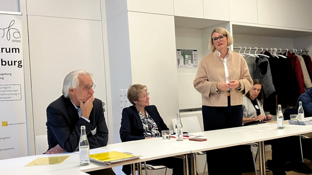 Begrüßung durch Eva Weber (Oberbürgermeisterin der Stadt Augsburg). Im Bild zu sehen auch Christoph Weller (Universität Augsburg), Ulrike Bahr (MdB bis 2025) und Dominique Pannke (Leiterin der Koordinierungsstelle des Kooperationsverbunds Demokratische Konfliktbearbeitung), v.l.n.r. sitzend.