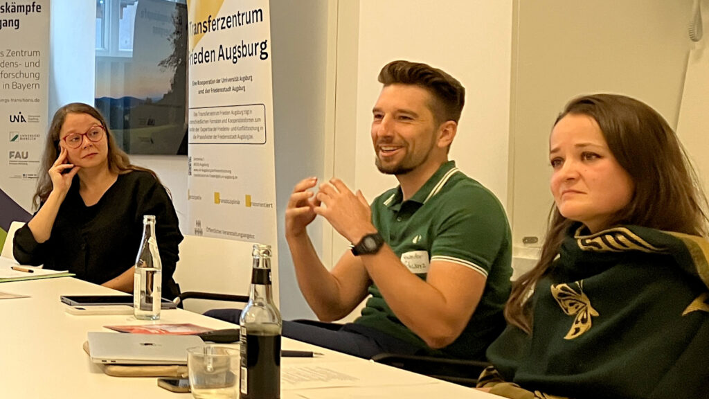 Alexander Schwarz (Universität Bayreuth) referiert zu der von ihm mitorganisierten Ausstellung als besonderes Transferformat des BZeFK. Neben ihm sitzen Michaela Zöhrer (links) und Christina Pauls (rechts), beide von der Universität Augsburg.